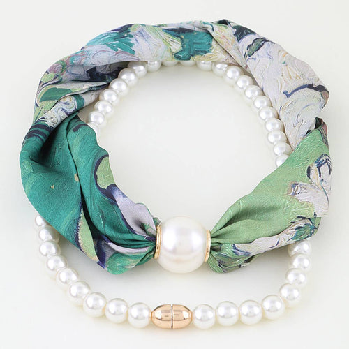 A pearl necklace layered with a silk scarf featuring a green, teal, and gray marbled pattern, tied with a central white pearl and accented by a rose gold clasp.