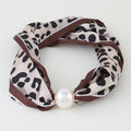 A leopard print silk scarf with brown trim and a large white faux pearl at the center, displayed on a clean white background.